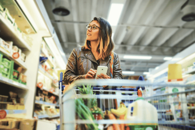 Woman looking at groceries in a grocery store with her phone in hand. 