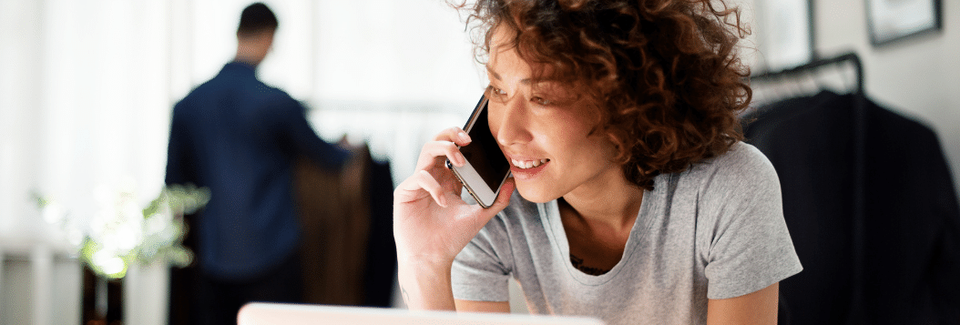 Woman leaning over desk with computer open and talking on her cellphone. 