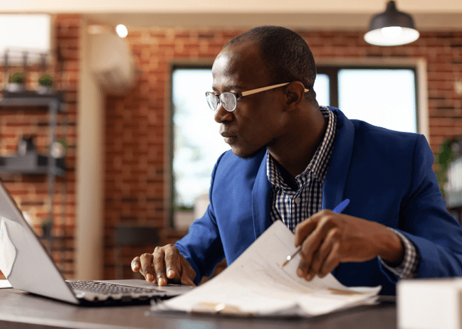 Middle aged Business man focusing intently on his laptop screen while flipping through documents. 