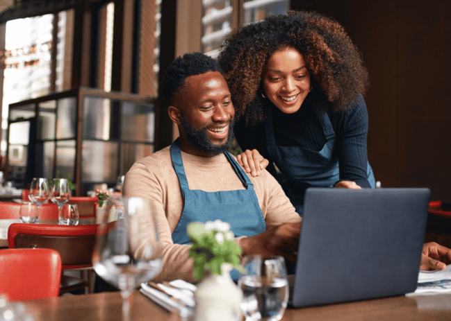 African American Couple looking at a computer smiling while sitting in their restaurant. 