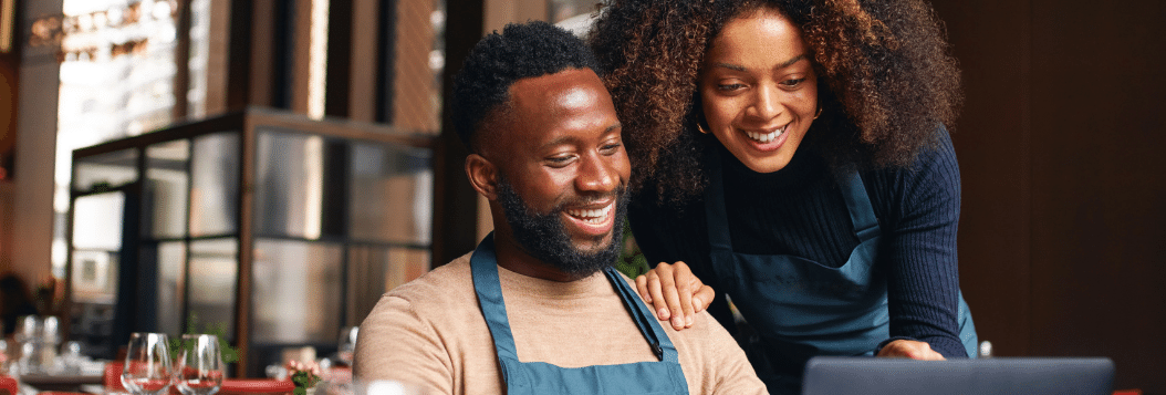 African American Couple looking at a computer smiling while sitting in their restaurant