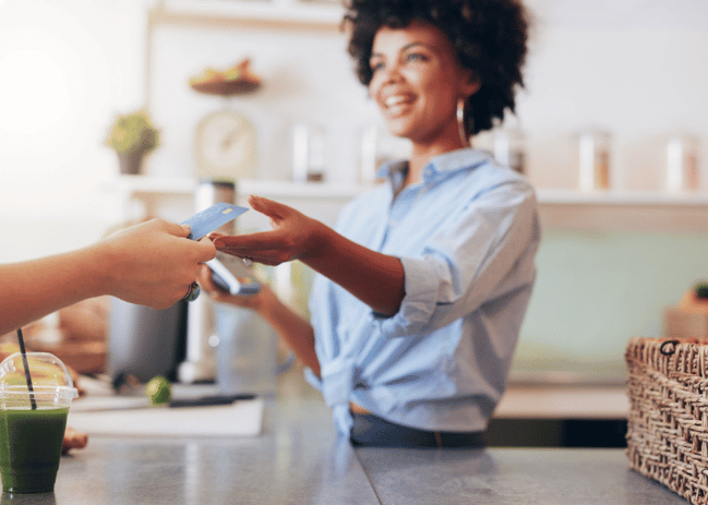 African America woman smiling while holding a card reader and grabbing a credit card from someone