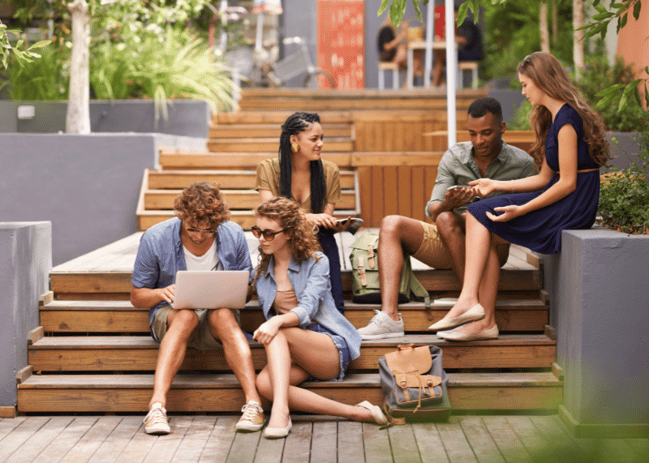 Young people sitting on wooden steps, engaged with their electronic devices