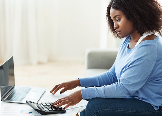 young black woman viewing online accounts and using calculator for budgeting