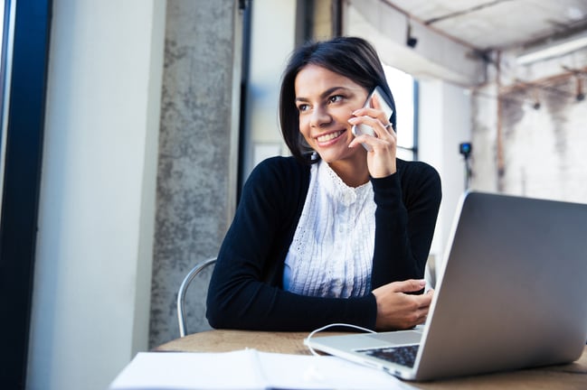 Happy businesswoman sitting at the table and talking on the phone in cafe. Looking away