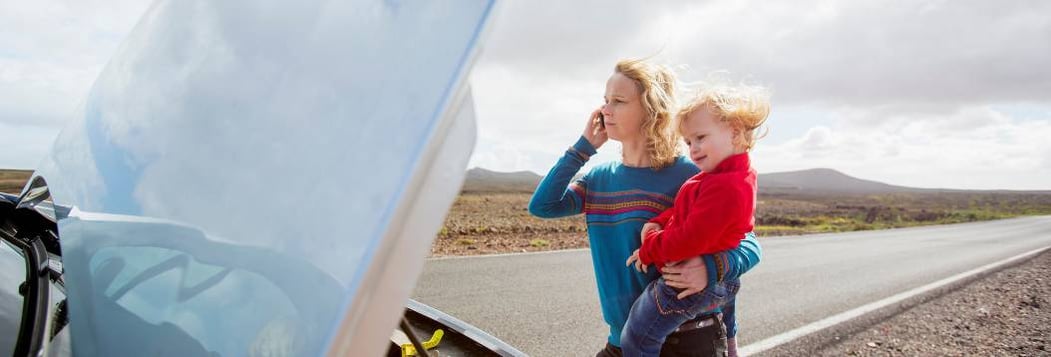 young mother with baby on hip broken down by side of the road