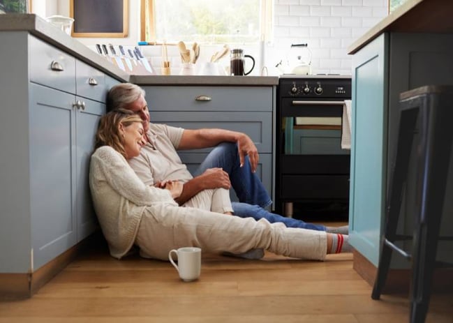 middle aged couple drinking coffee sitting on kitchen floor