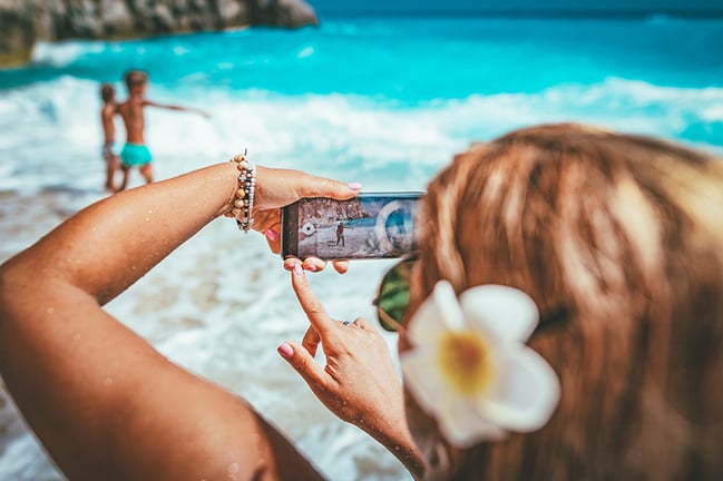 mom taking photos of kids on family vacation at beach