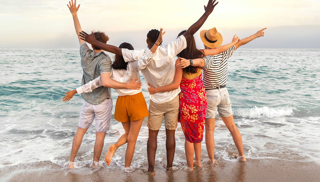 A group of young people at the beach with their feet in the water and arms around each other. 
