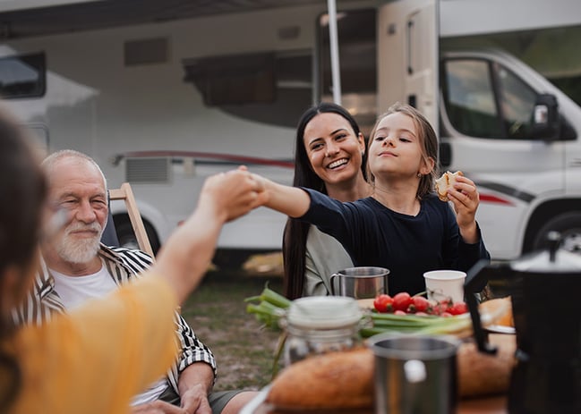 Family gathered around RV eating dinner outside