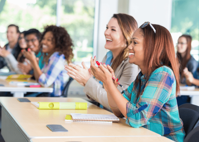 Smiling young people sitting at long tables and clapping