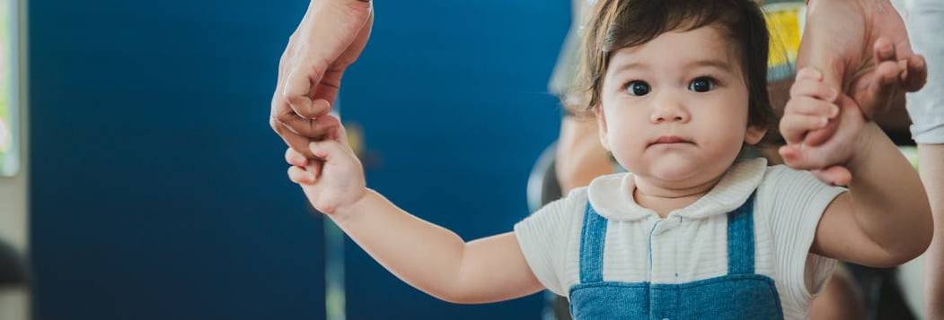 girl toddler taking first step while holding hands of parent