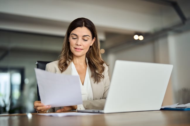 Lady looking at a paper with her laptop open