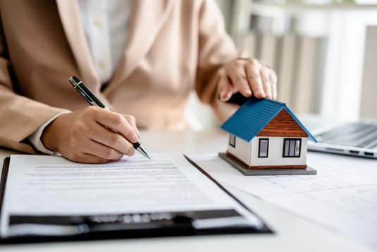 Person writing while holding a model of a house