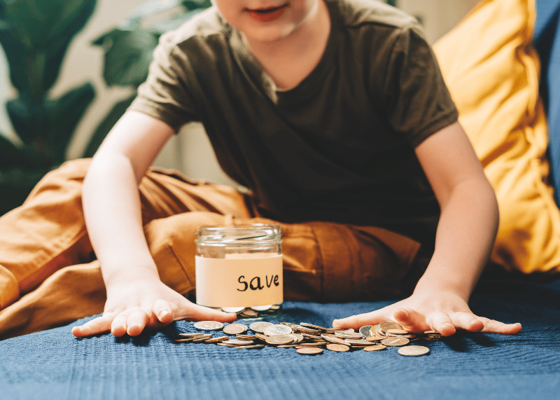 Child saving coins in jar labeled savings